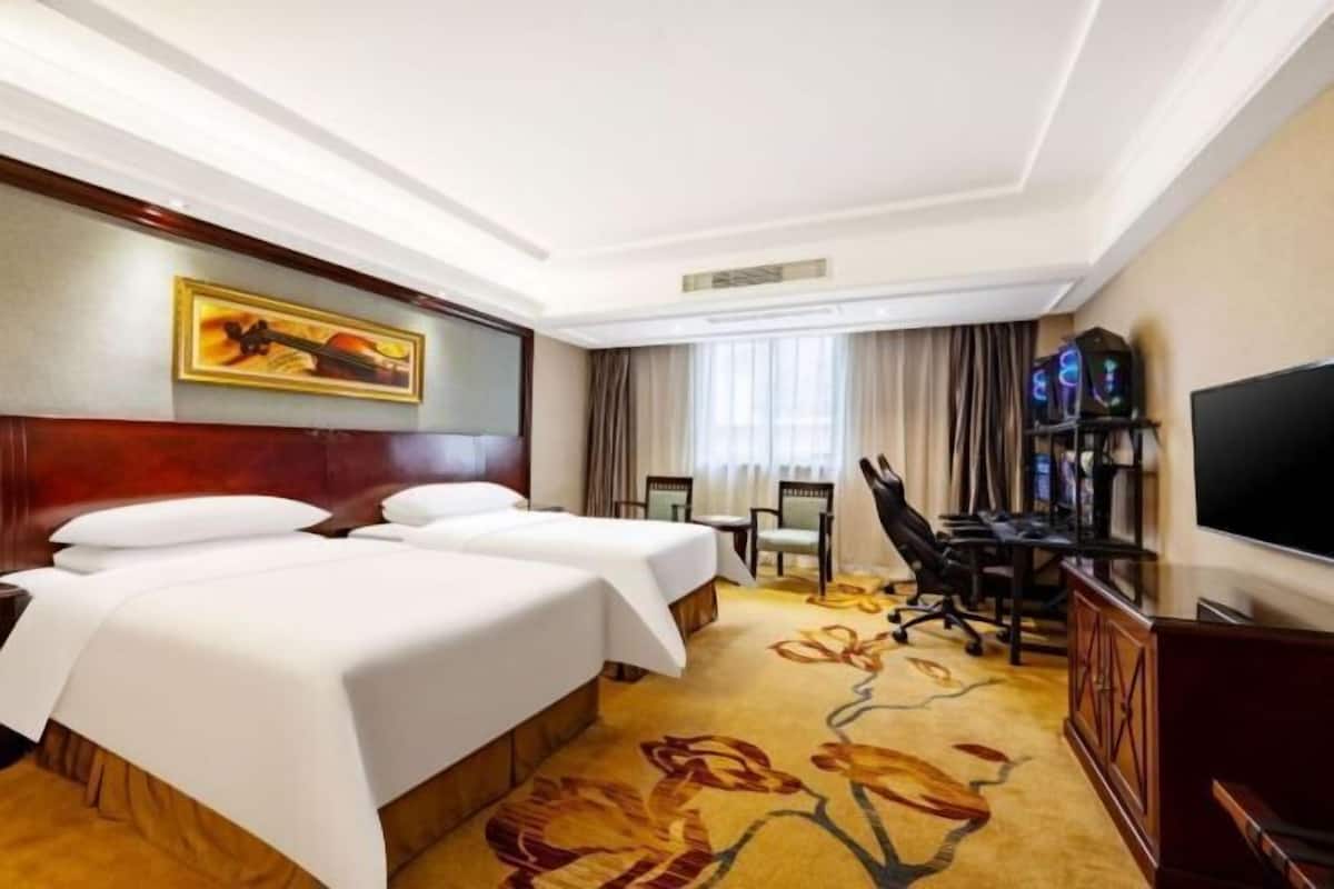 A hotel room with two beds, a desk, a chair, a television, and a painting on the wall.