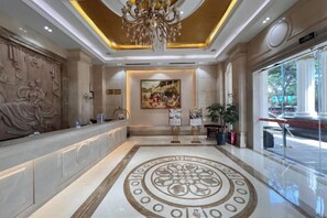 Un vestíbulo con una mesa de recepción, una araña, un cuadro grande y un piso con diseño.