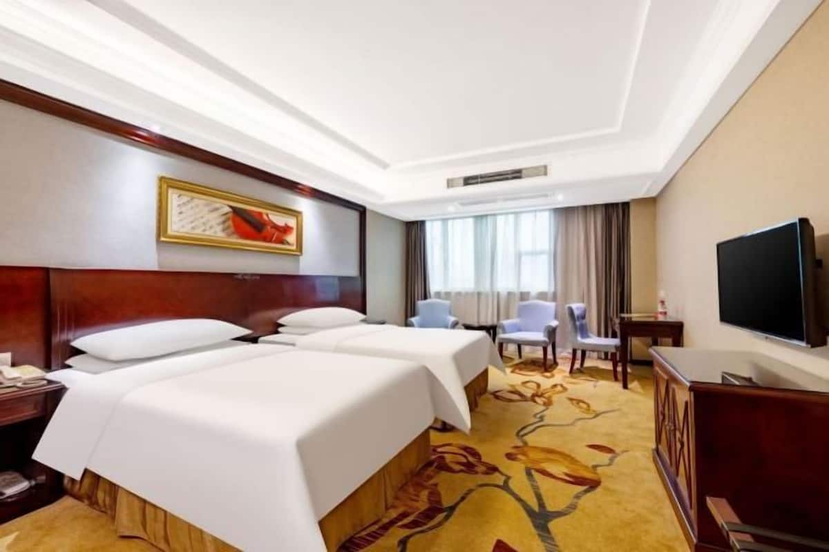 A hotel room with two beds, a TV, a desk, and a chair.