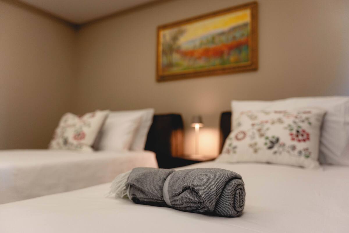 A hotel room with two beds, a painting on the wall, and a lamp.