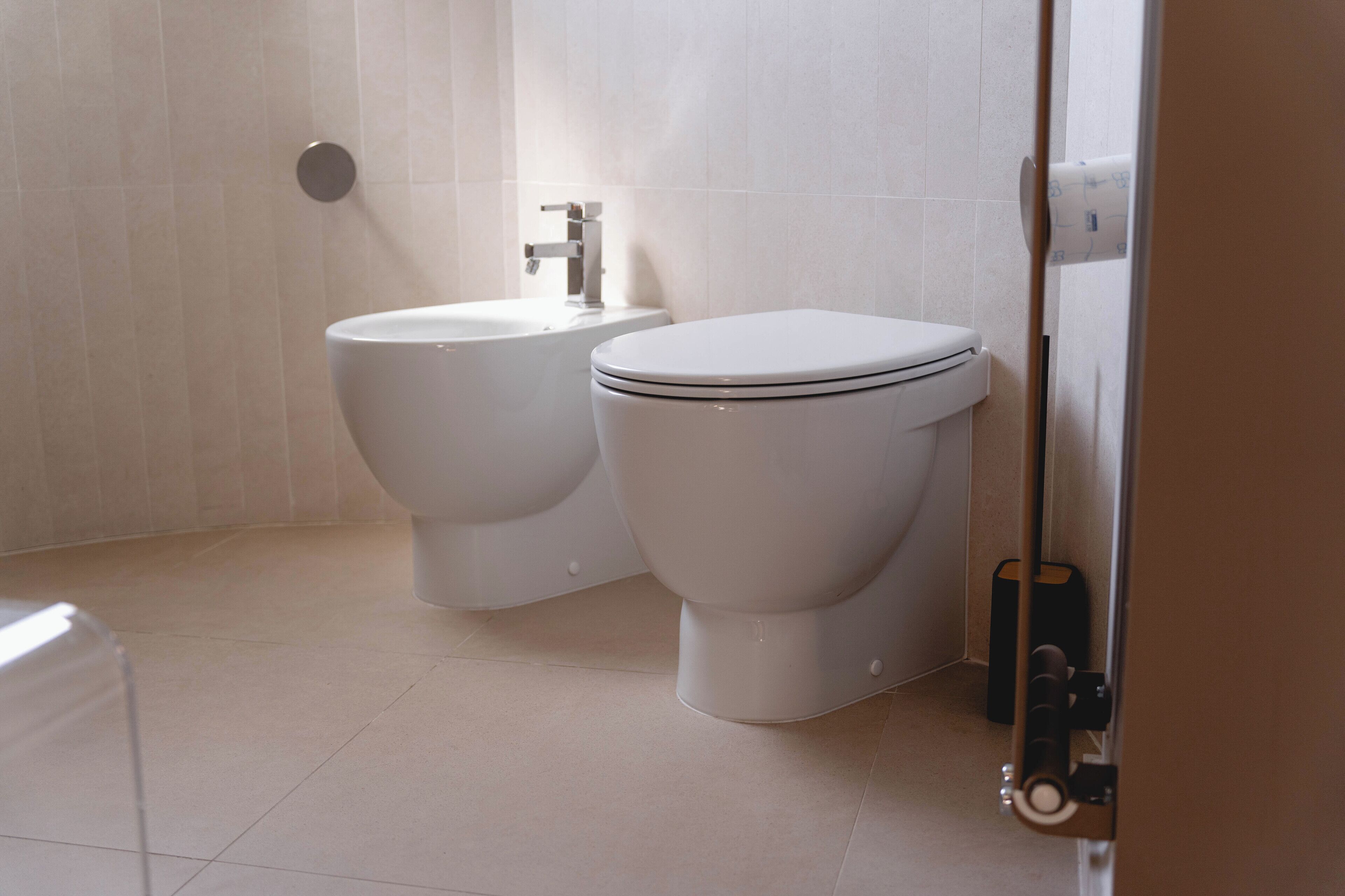 A bathroom with two toilets, a sink, and a toilet paper holder.