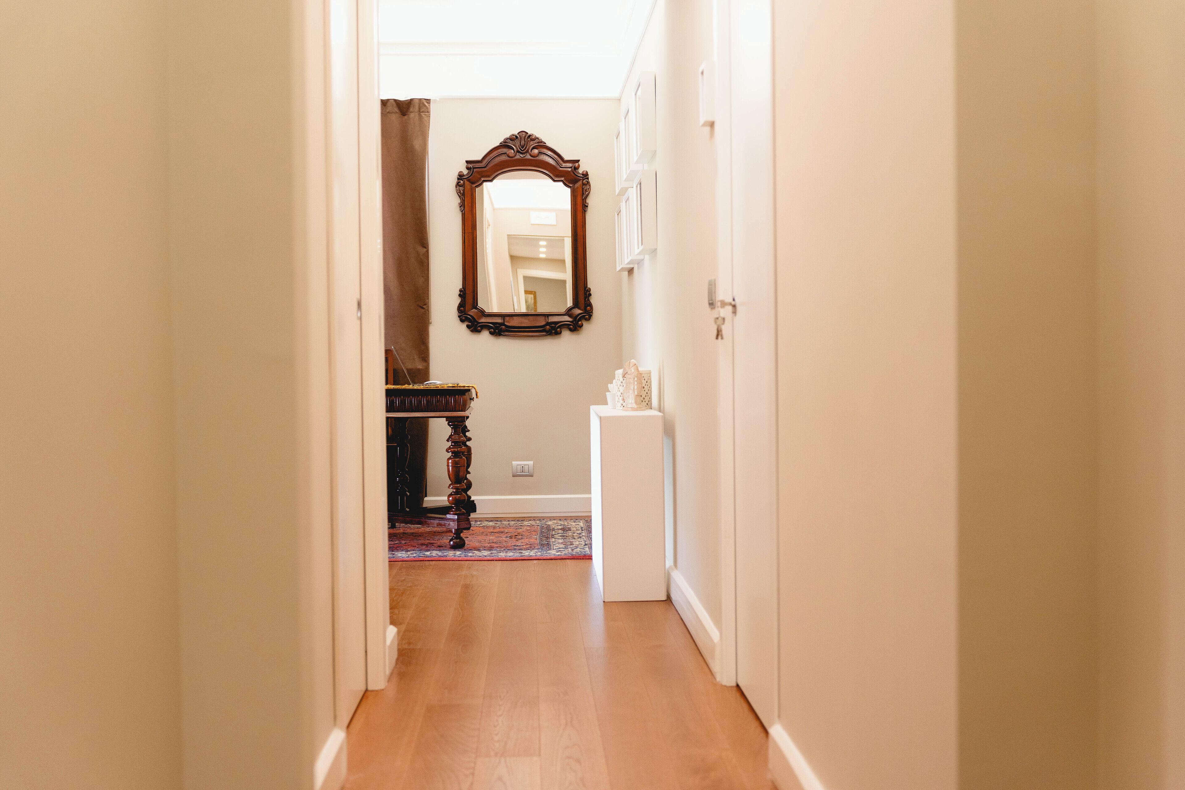 A hallway with wooden flooring, a mirror on the wall, and a door at the end.