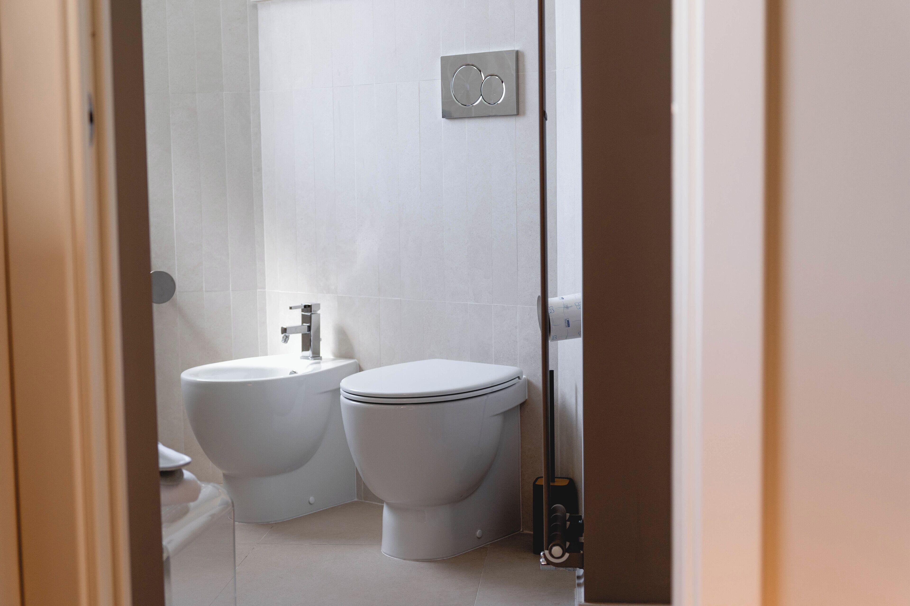 Een moderne badkamer met toilet, bidet en een wandtoiletrolhouder.