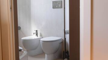 Un baño moderno con inodoro, bidé y dispensador de papel higiénico en la pared.