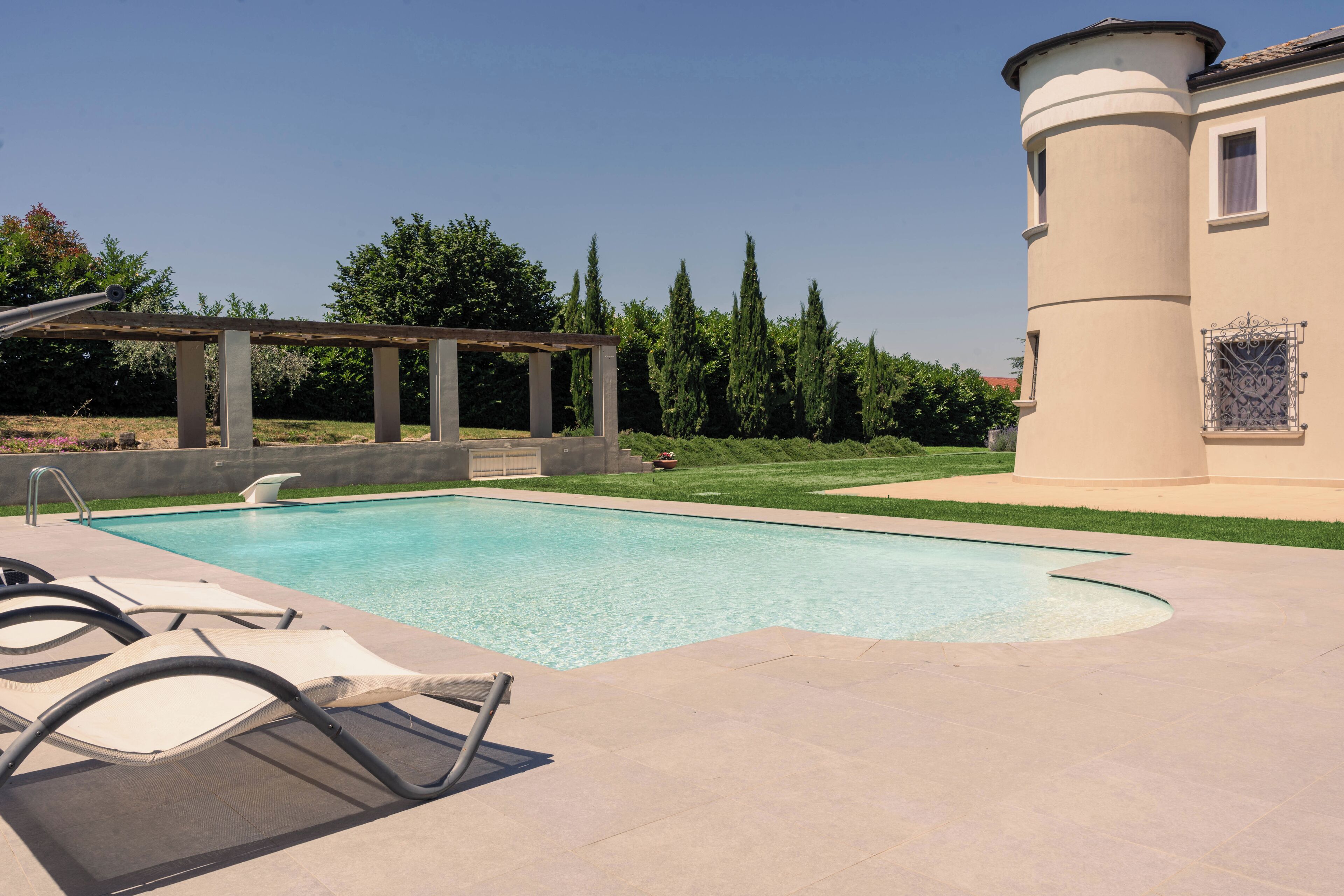 Ein Swimmingpool mit Liegestühlen, einer Pergola und einem Gebäude mit einem runden Turm.