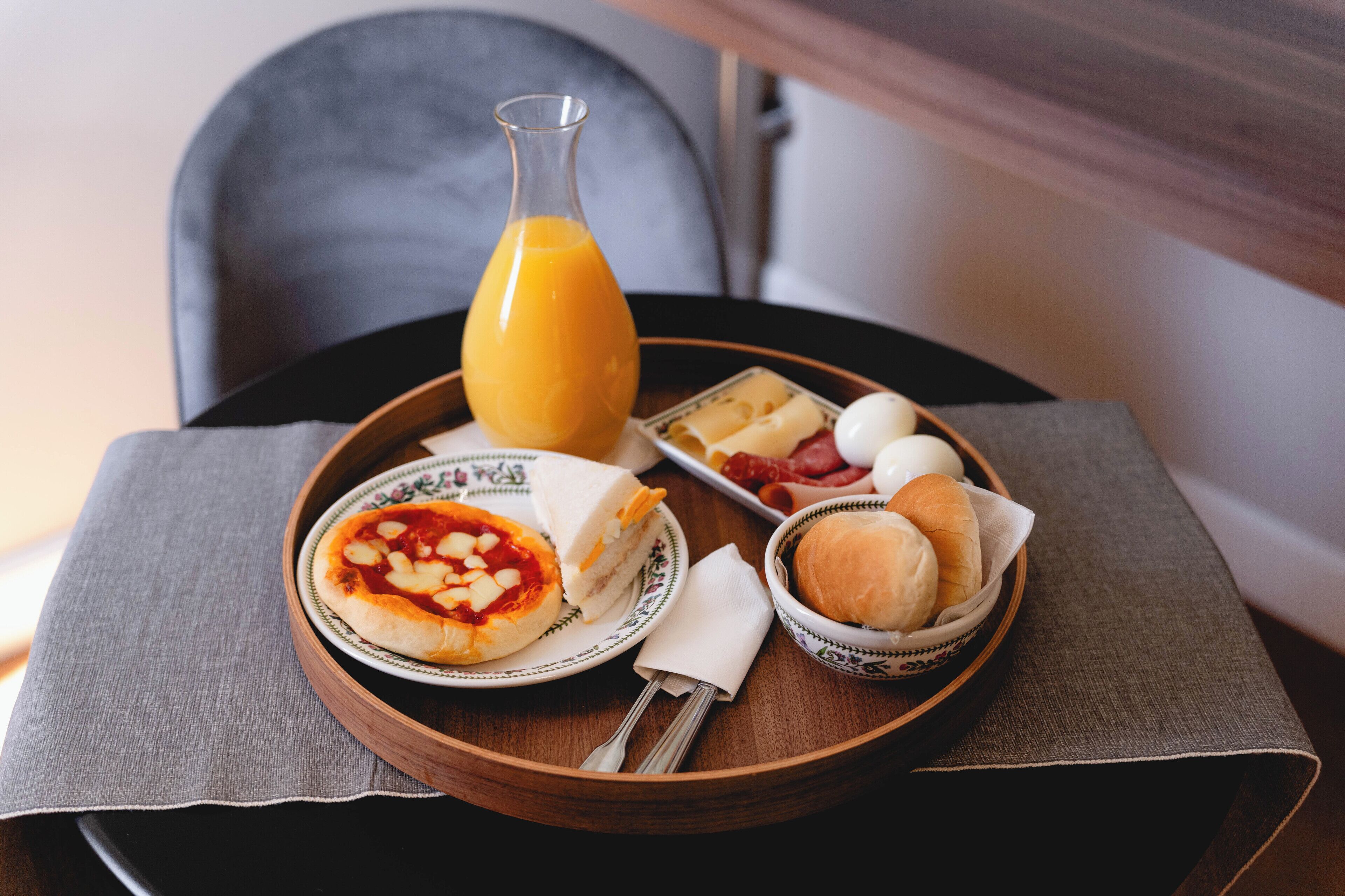 A breakfast tray with a pizza, eggs, bread, and a bottle of orange juice on a table.