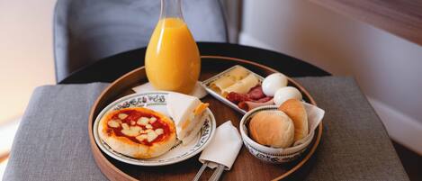 Bandeja de desayuno con pizza, huevos, pan y una botella de jugo de naranja sobre una mesa.