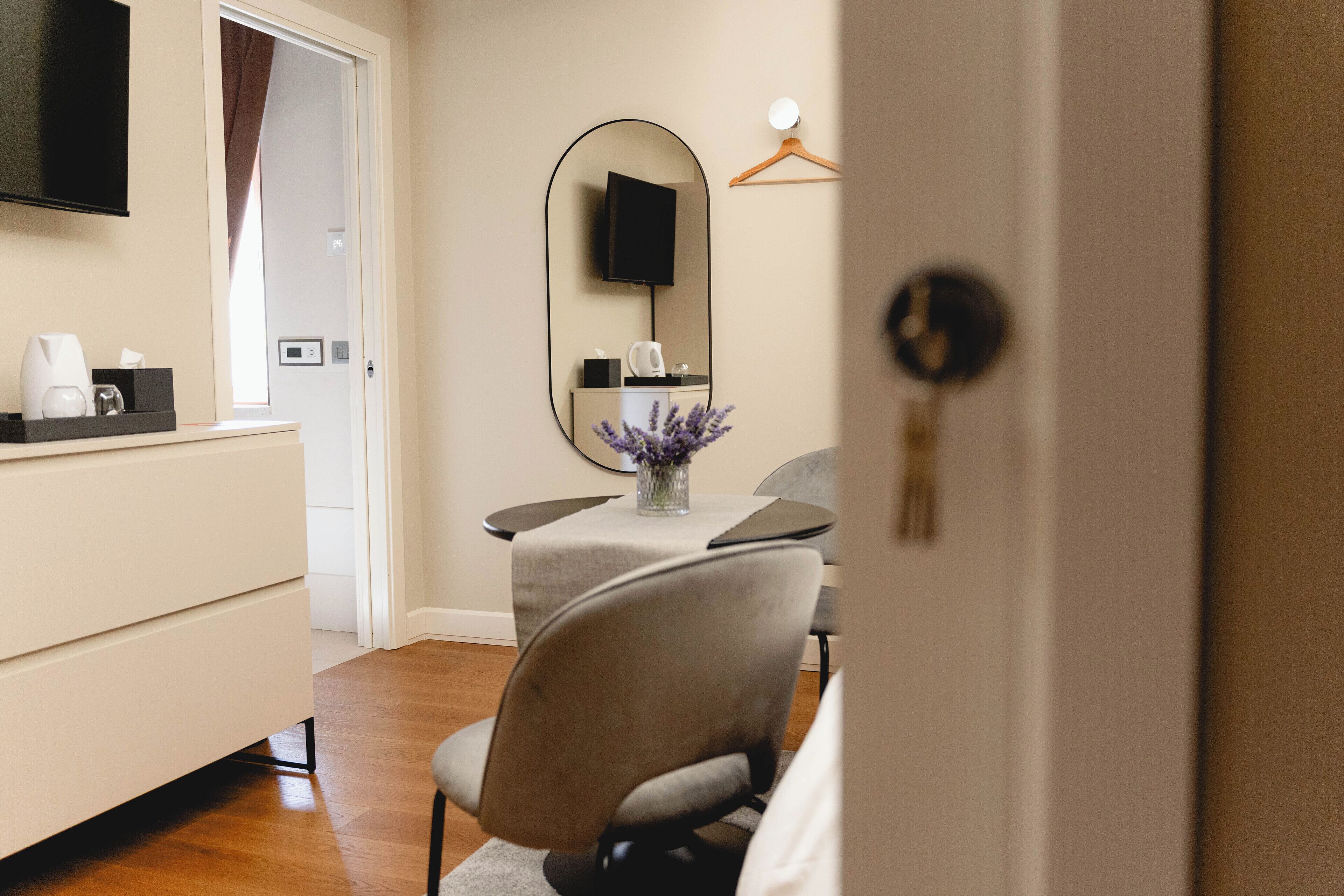 A hotel room with a bed, a bedside table, a TV, a mirror, and a door.