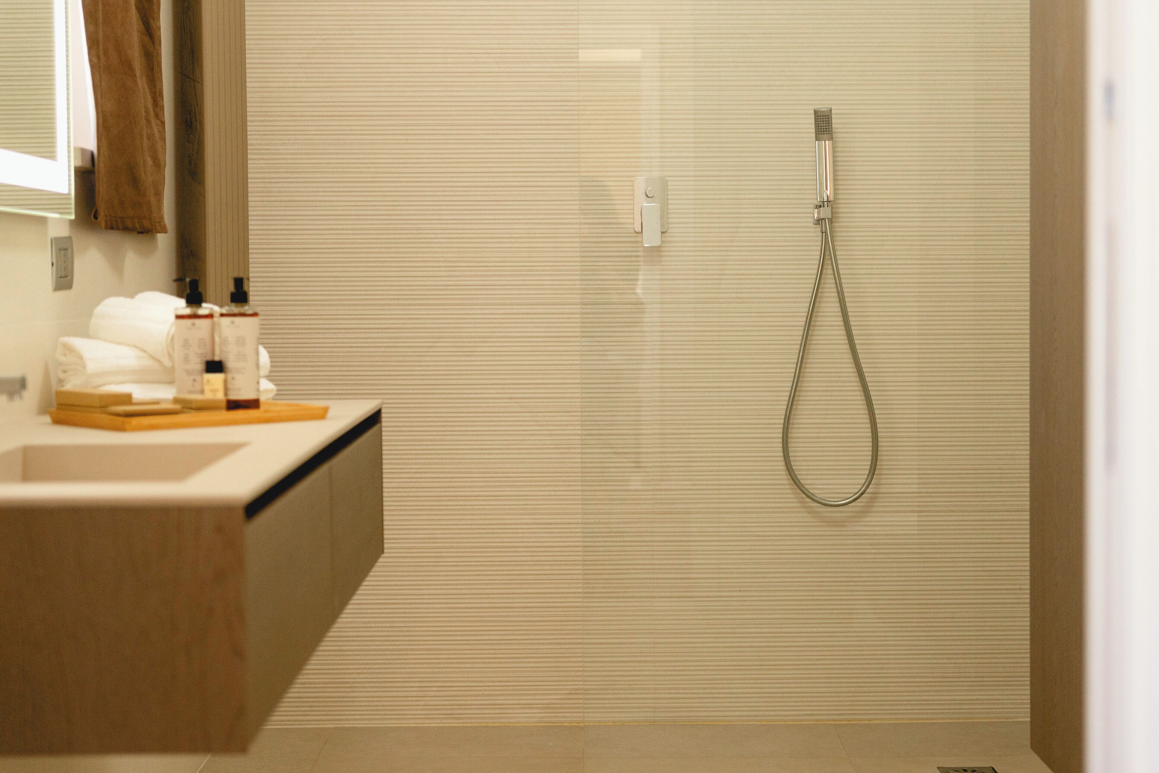 A modern bathroom with a glass-enclosed shower, a wooden vanity with toiletries, and a towel rack.