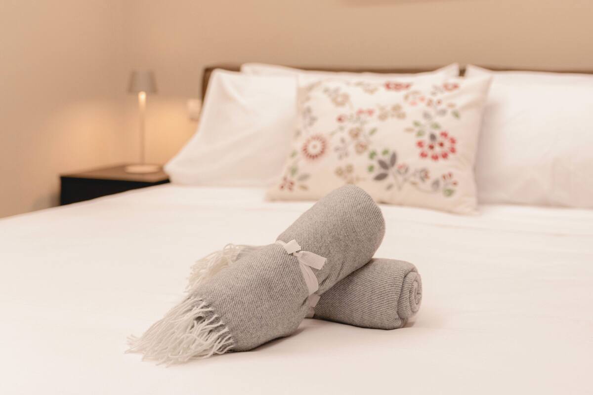 A neatly made bed with a rolled towel and a floral pillow.