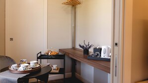 A neatly arranged room with a dining table set for tea, a small shelf with a coffee maker, and a wooden hanger rack. - Ayma B&B (Mirabella Eclano)