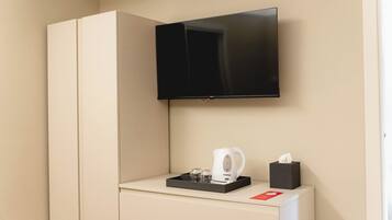 A hotel room with a flat-screen TV mounted on the wall, a minibar with a coffee maker, and a tissue box.