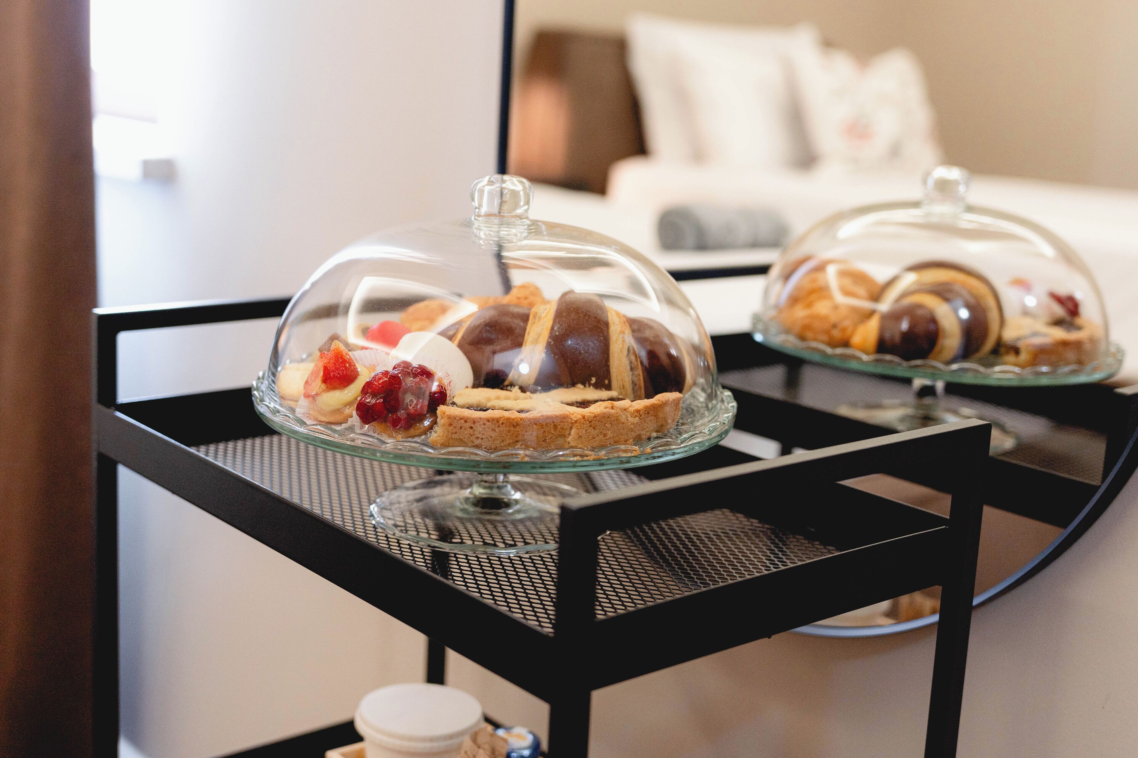 Ett glassmontr med bakverk och desserter står på ett svart metallbord i ett hotellrum.