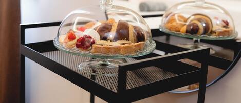 A glass display case with pastries and desserts on a black metal table in a hotel room.