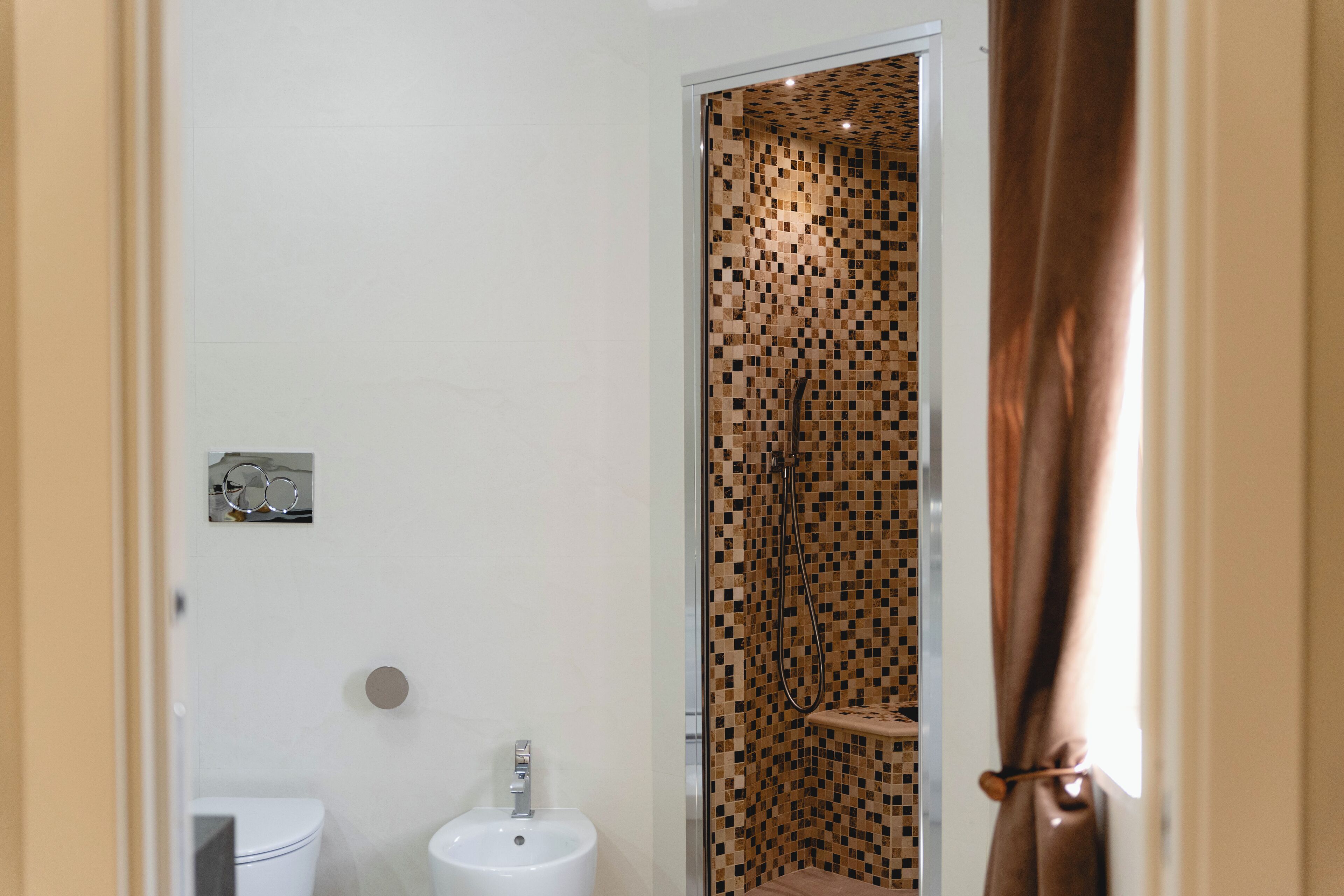 Une salle de bain avec un lavabo blanc, des toilettes et une douche dont le mur est recouvert de mosaïques.