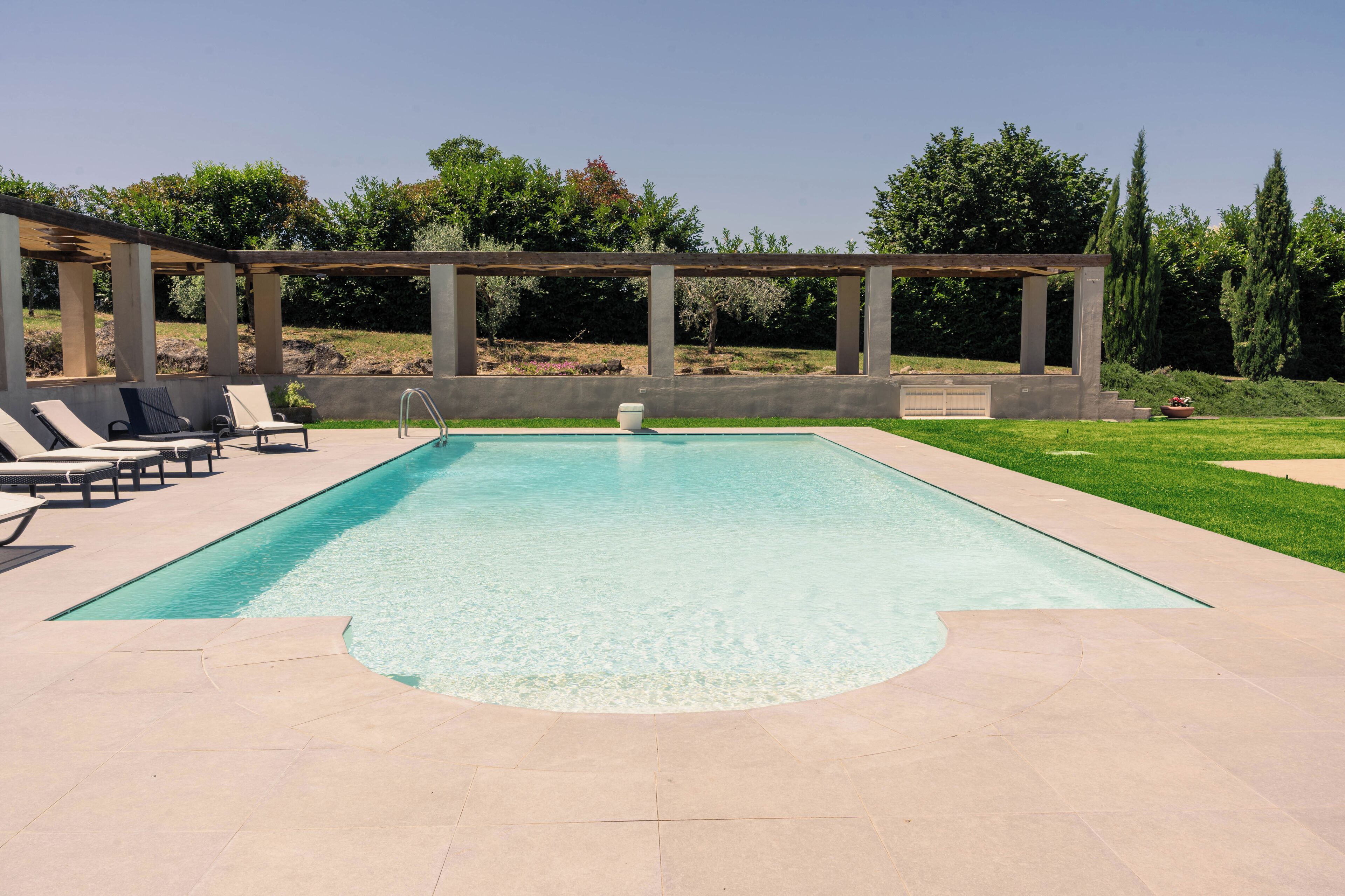 Une piscine rectangulaire agrémentée d’une pergola et de chaises longues.