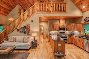 A spacious living area with a wooden staircase, a kitchen with modern appliances, and a dining area. - Beech Creek Cabin (Banner Elk)