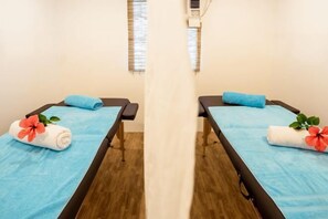 Due lettini per massaggi con lenzuola e asciugamani azzurri, ciascuno decorato con un fiore.