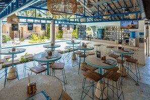 Un'ampia caffetteria all'aperto con tavoli e sedie rotonde, un'area bar e vista sulla piscina e sul verde.