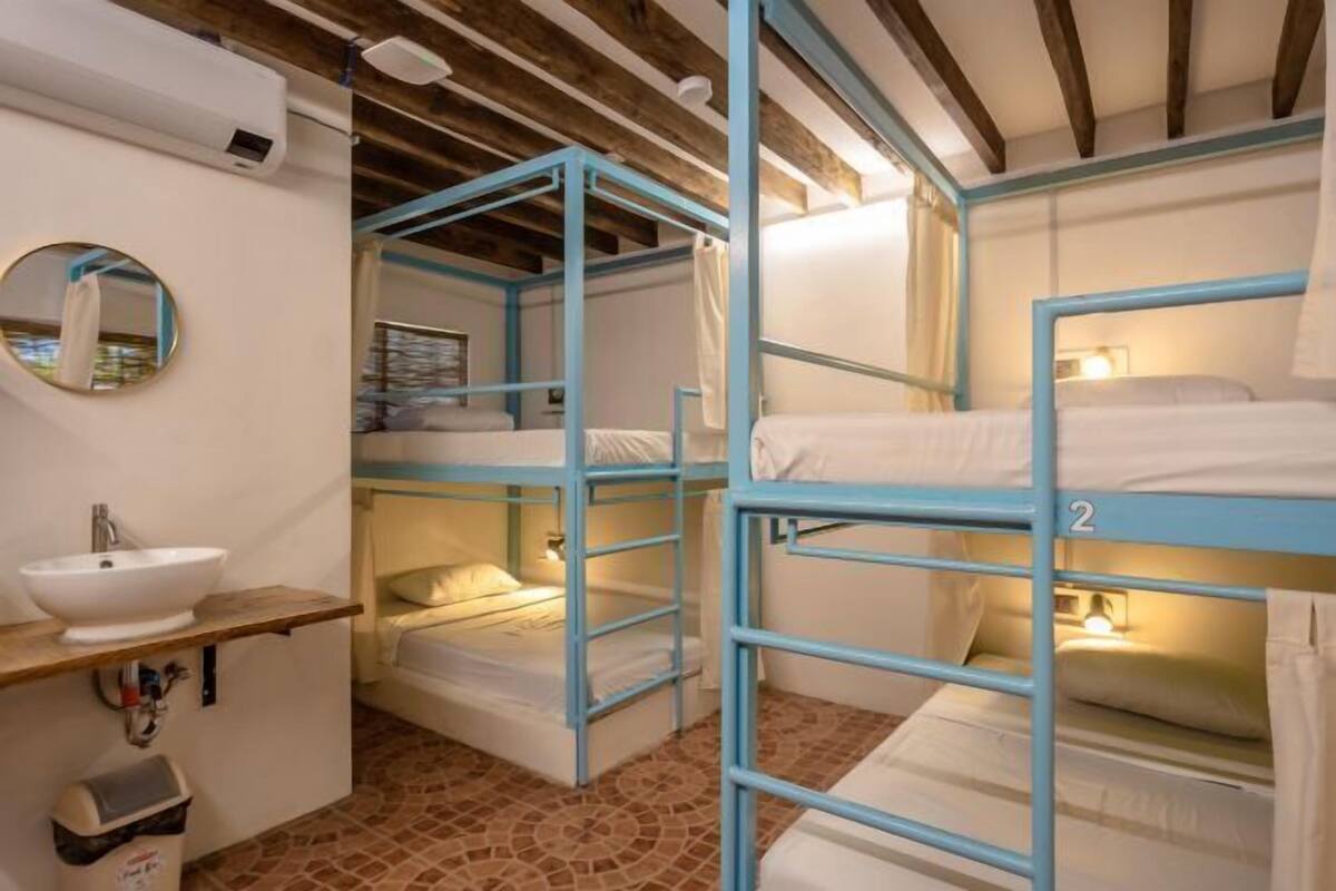 A bunk bed room with a sink and mirror, wooden beams on the ceiling, and a tiled floor.