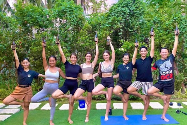 A group of people in a garden setting, possibly engaged in a yoga or fitness class.