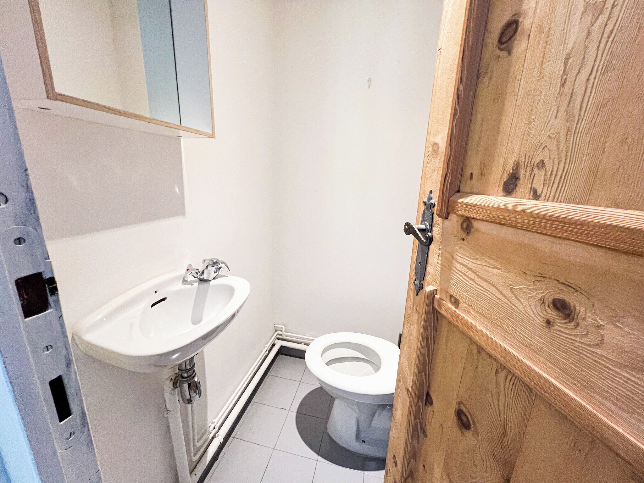 A small bathroom with a white sink, a toilet, and a wooden door.
