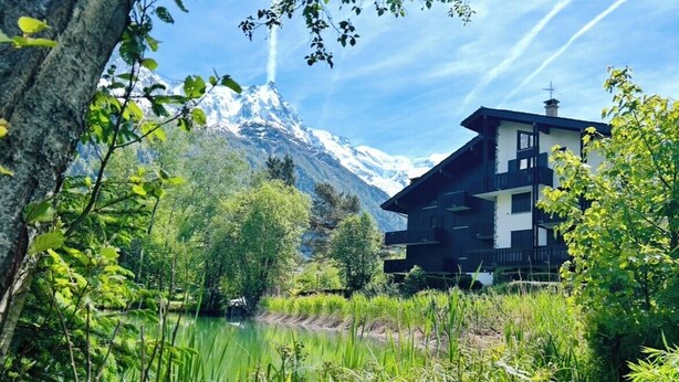 A mountain lodge with a view of snow-capped peaks, surrounded by lush greenery and a calm lake. - Appt in Mont Blanc view and parking (Chamonix-Mont-Blanc)
