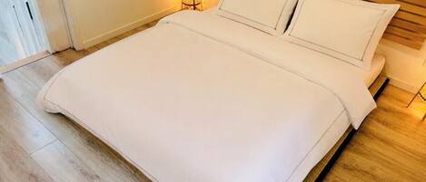 A neatly made bed with a wooden headboard, a bedside lamp, and a wooden floor.