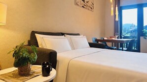 A hotel room with a bed, a small table with a plant and a mug, a painting on the wall, and a view through the window. - Appt in Mont Blanc view and parking (Chamonix-Mont-Blanc)
