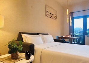 Une chambre d’hôtel avec un lit, une petite table sur laquelle se trouvent une plante et une tasse, un tableau au mur et une vue par la fenêtre.