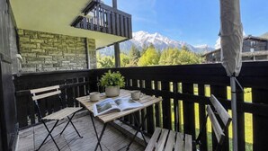 A wooden deck with a table, chairs, and a book, overlooking a mountain landscape. - Appt in Mont Blanc view and parking (Chamonix-Mont-Blanc)
