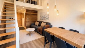 A modern interior with a wooden staircase, a dining area with a table and chairs, a sofa, and a painting on the wall. - Appt in Mont Blanc view and parking (Chamonix-Mont-Blanc)