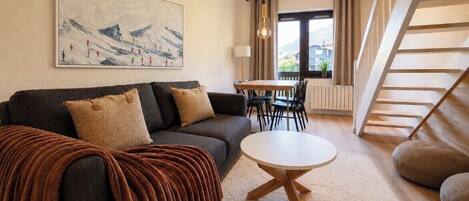 A modern living room with a sofa, a round table, a painting, and a staircase.