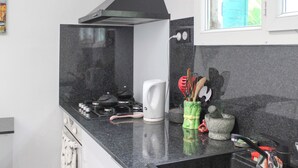 Una cocina con estufa a gas, una tetera blanca y varios utensilios en un organizador.