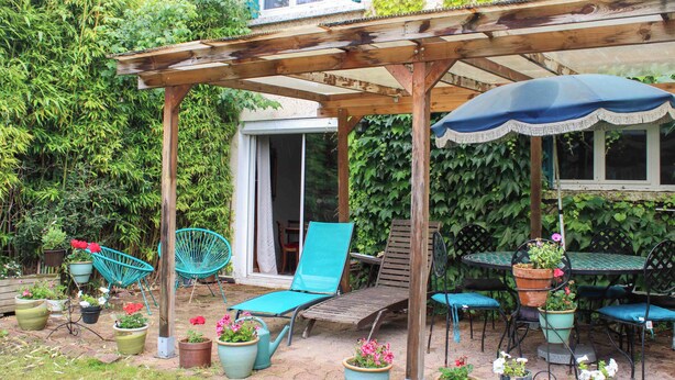 Un área de patio techada con mobiliario de madera, plantas en macetas y una estructura de pérgola.