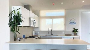 Een moderne keuken met witte kasten, een centraal eiland met barkrukken, een magnetron en een spoelbak.