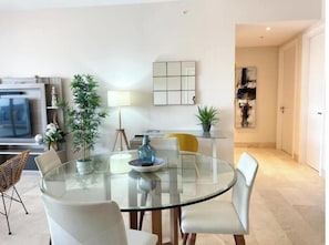 A modern living room with a glass dining table, white chairs, a TV, and decorative plants. - Nautical Escape 2BR Marina View (Río Hato)