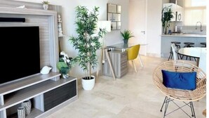 Een moderne woonkamer met een flatscreen televisie, een eethoek met een gele stoel, en een keuken met een wit aanrecht.
