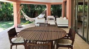 Relax in style with a round table and four cushioned chairs, a sofa, and a hammock amidst lush greenery.