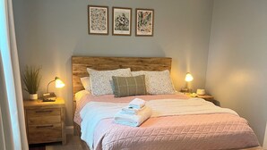 A bedroom with a wooden bed, two bedside tables, a nightstand, a wall-mounted lamp, and framed botanical prints. - Cozy sunlit apartment steps from downtown Dover. Parking included (Rollinsford)