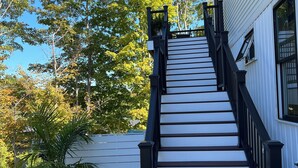 A staircase leading to a white building with black railings, surrounded by trees and a potted plant. - Cozy sunlit apartment steps from downtown Dover. Parking included (Rollinsford)