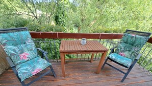 Une terrasse en bois avec deux chaises et une table, entourée de verdure.