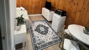 A compact living space with a wooden wall, a white sofa, a dining table with chairs, a small refrigerator, and a TV on a wooden cabinet. - More then a Motel With Garden , Renovated Rooms at heart of Boothbay (Boothbay)
