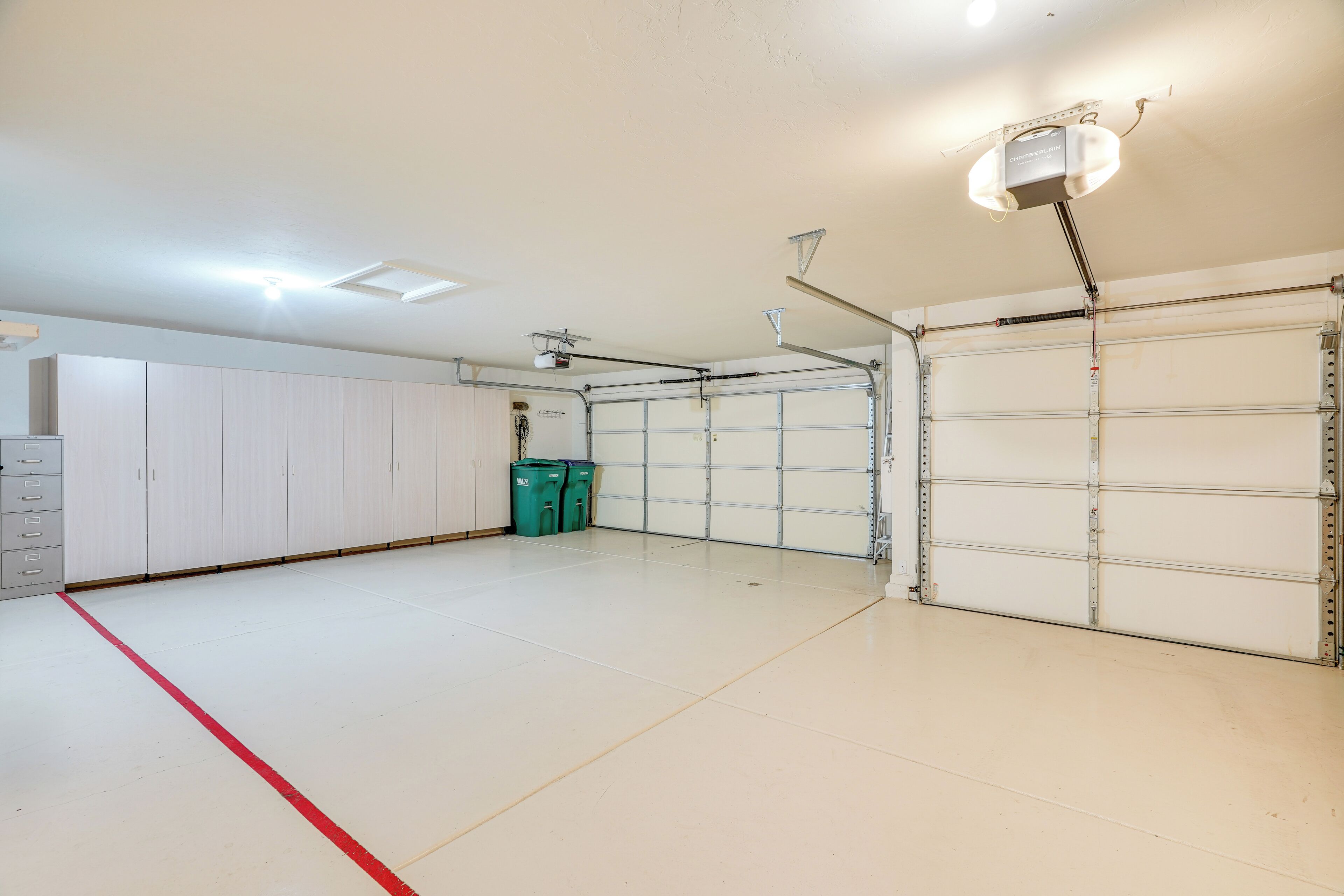 A spacious garage with white walls, a red line marking the floor, and two green dumpsters.