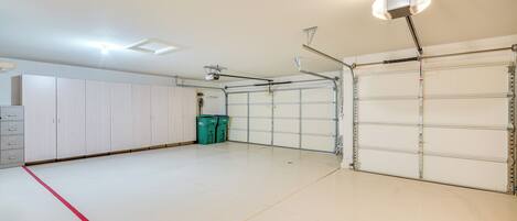 A spacious garage with white walls, a red line marking the floor, and two green dumpsters.