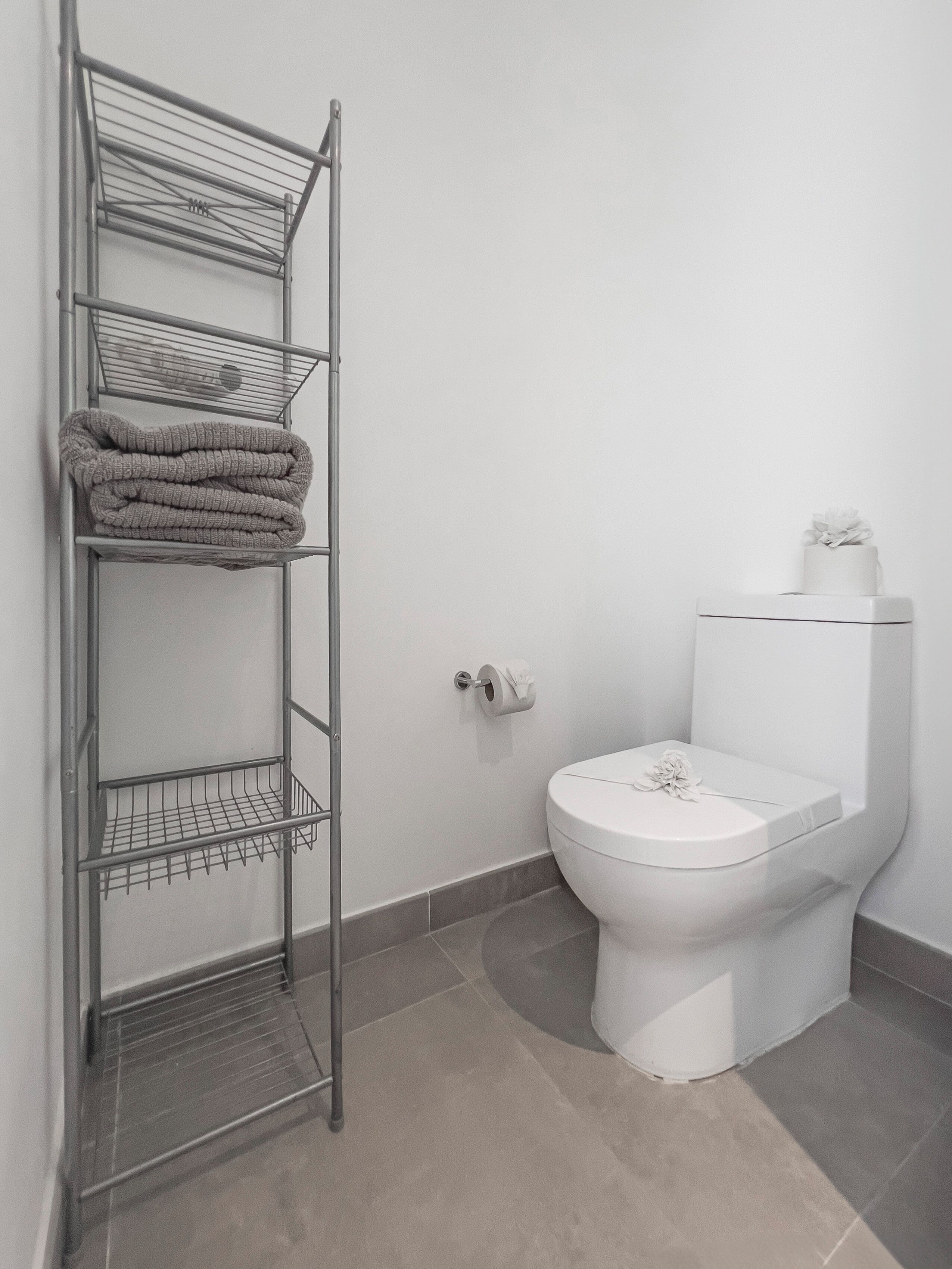 A bathroom with a metal towel rack holding folded towels, a toilet with a tissue box on top, and a toilet paper holder on the wall.
