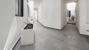 A modern, narrow hallway with white walls and grey tiled flooring. There are potted plants along the left wall and a visible fire extinguisher on the right. - Quinto Sol Tulum (Tulum)