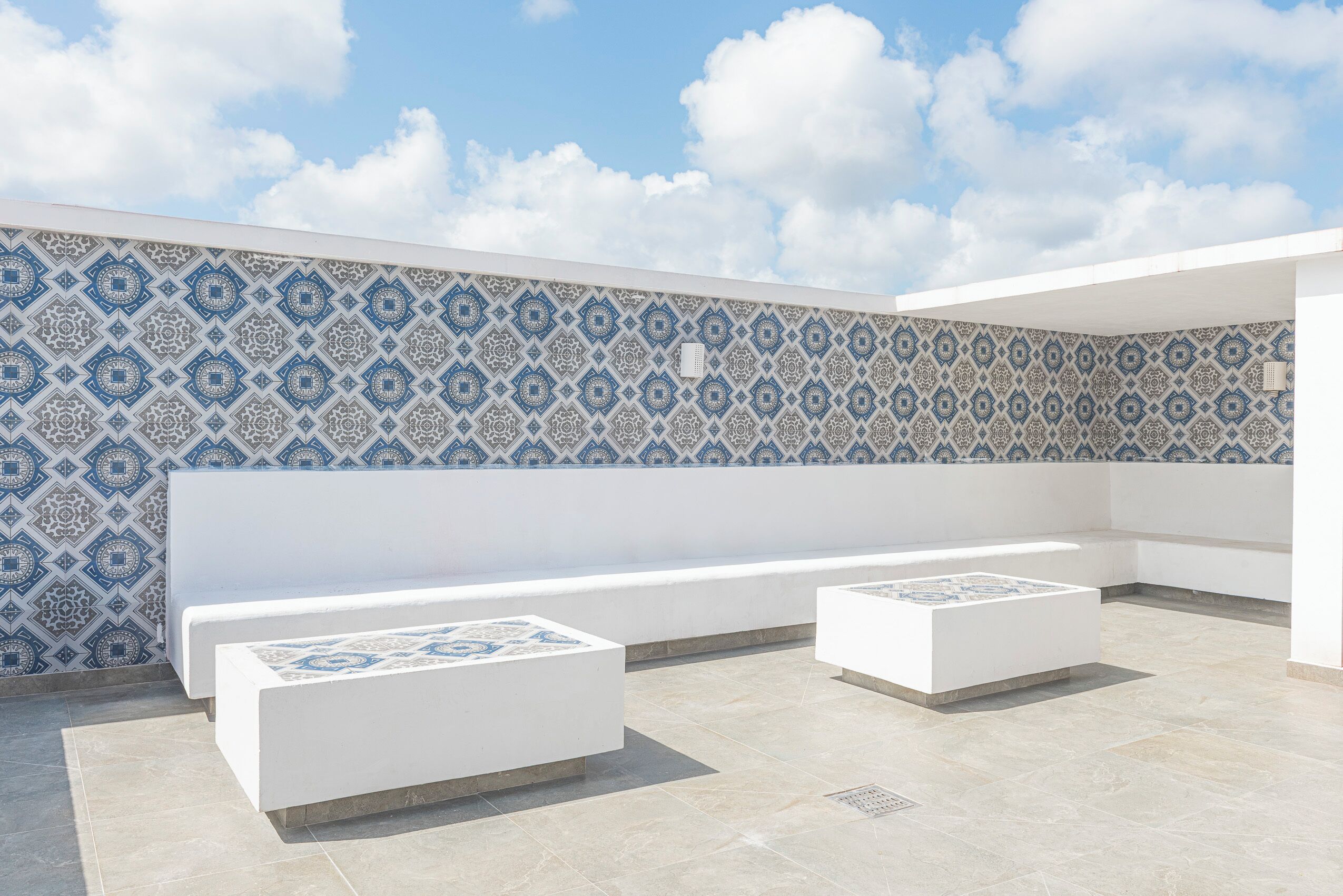 A rooftop terrace with patterned tiles, white seating, and a clear sky.
