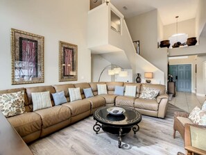 A spacious living room with a large L-shaped sectional sofa, a round coffee table, and a staircase leading to an upper level. - Near Disney - Free WIFI - Gated Community - Golf Course (Haines City)