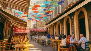 Un café en plein air avec des tables et des chaises, une allée couverte et des parasols colorés suspendus au plafond.